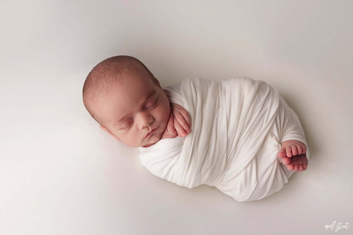newborn baby swaddled in white wrap photographed by april stout photography near Jenks Oklahoma