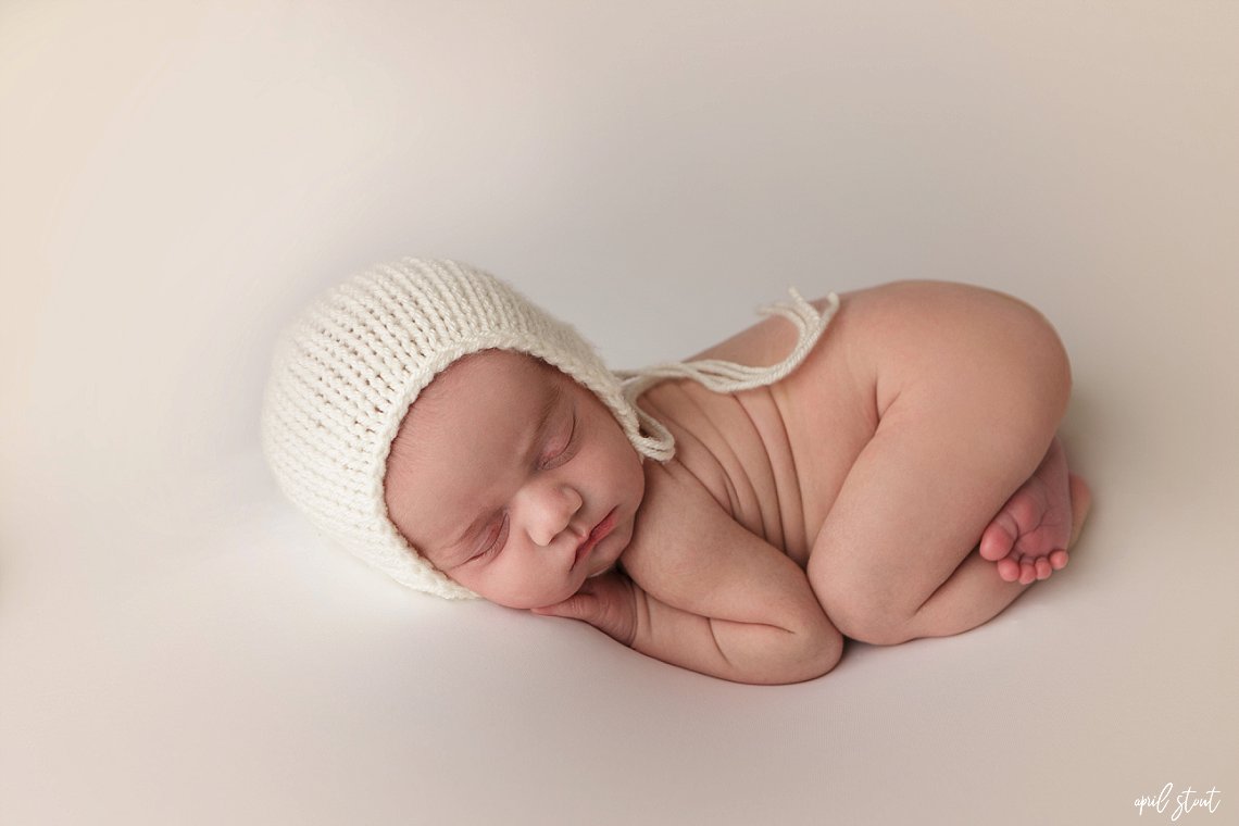 new baby boy in studio with April Stout Photography captured on a simple white backdrop with a little bonnet