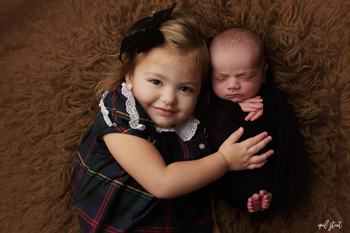 big sister with newborn baby brother on brown fur captured by April Stout photography