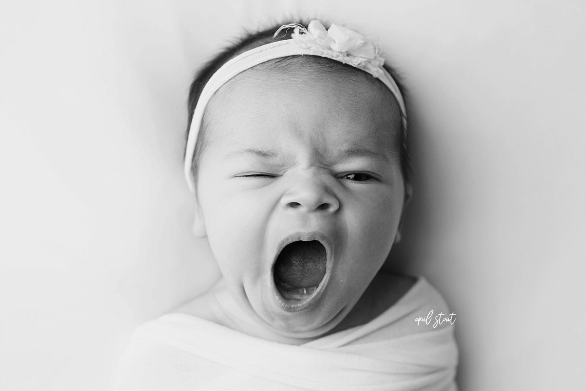 baby girl yawning on simple white backdrop by april stout newborn photographer
